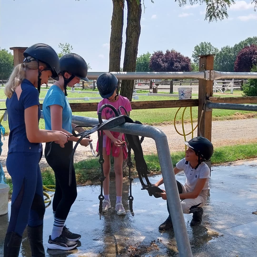 Bambini impegnati nella pulizia dell'attrezzatura durante il campo estivo al Circolo Ippico Tara